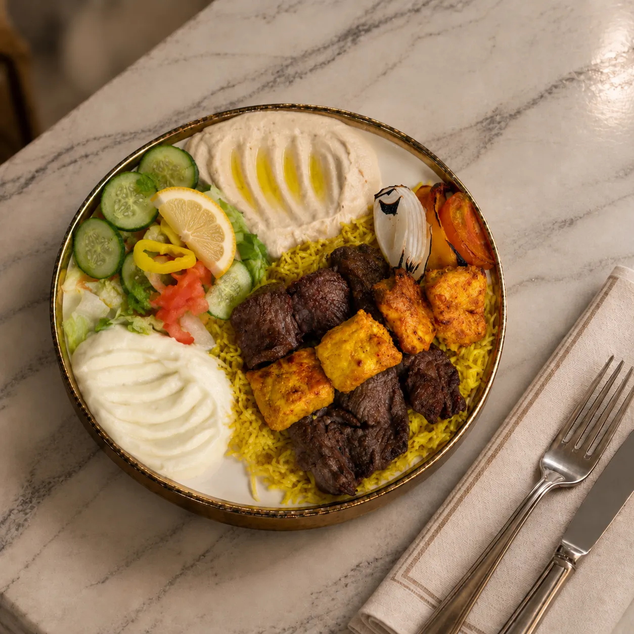 Mixed grill plate with beef kabob and chicken tawook on rice with hummus and garlic sauce