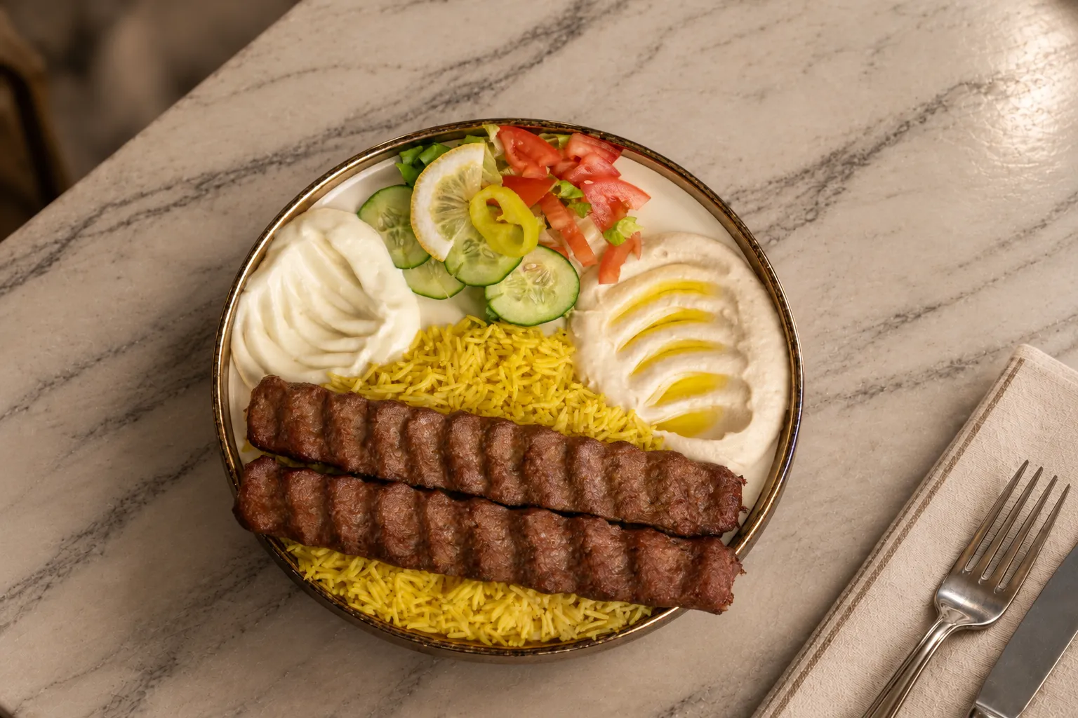 Kafta kabob plate with two skewers on yellow rice, hummus, garlic sauce and salad